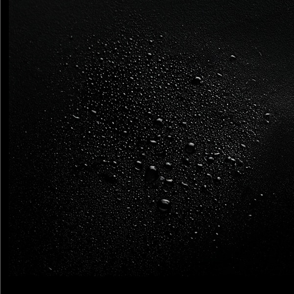 Dark, matte surface scattered with numerous small water droplets of varying sizes.